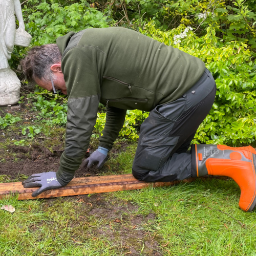 Mand nede på jorden med handsker som udfører havearbejde i Slagelse med rive i jorden.