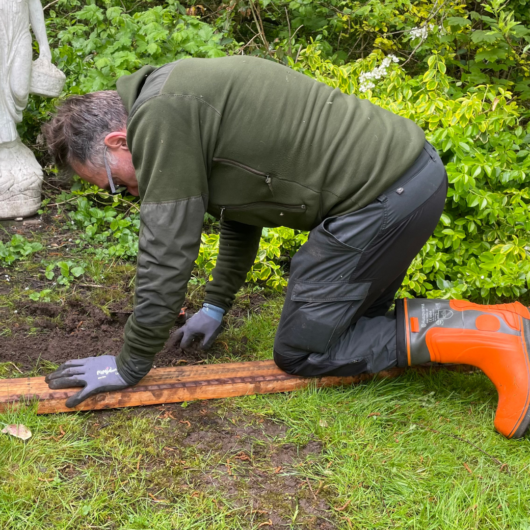 Mand nede på jorden med handsker som udfører havearbejde i Slagelse med rive i jorden.